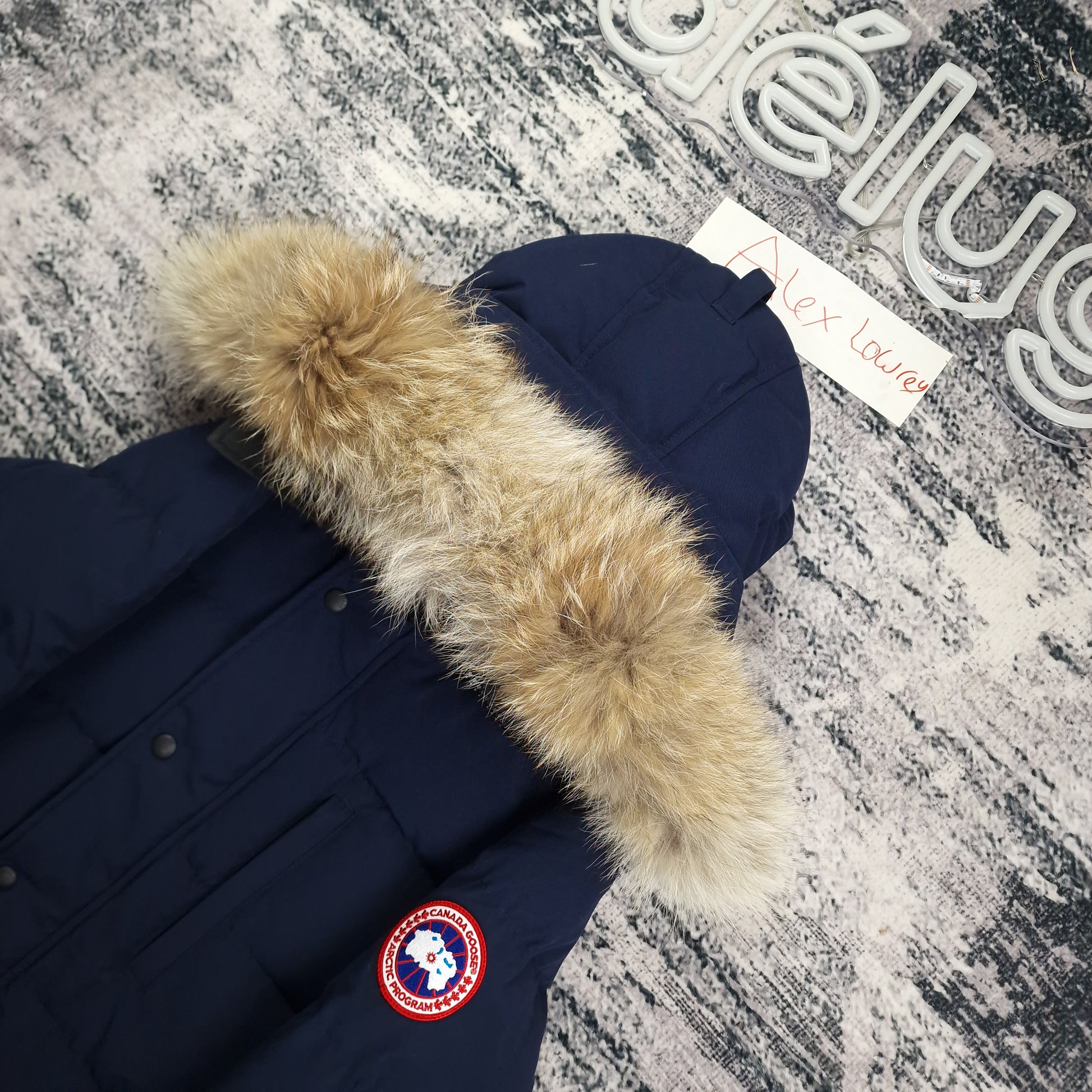 Close-up flat lay of Canada Goose Carson Parka 3805MA showing luxurious coyote fur hood trim and Arctic Program disc badge in admiral blue