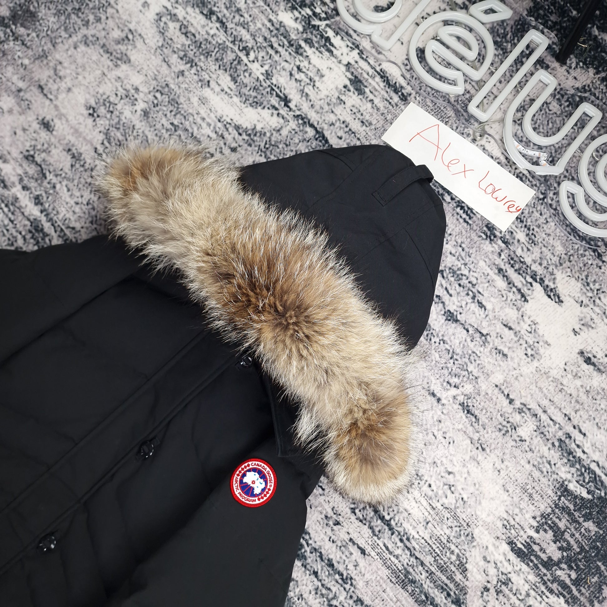 Close-up flat lay of Canada Goose Lorette Parka black showing coyote fur hood trim and Arctic Program disc badge