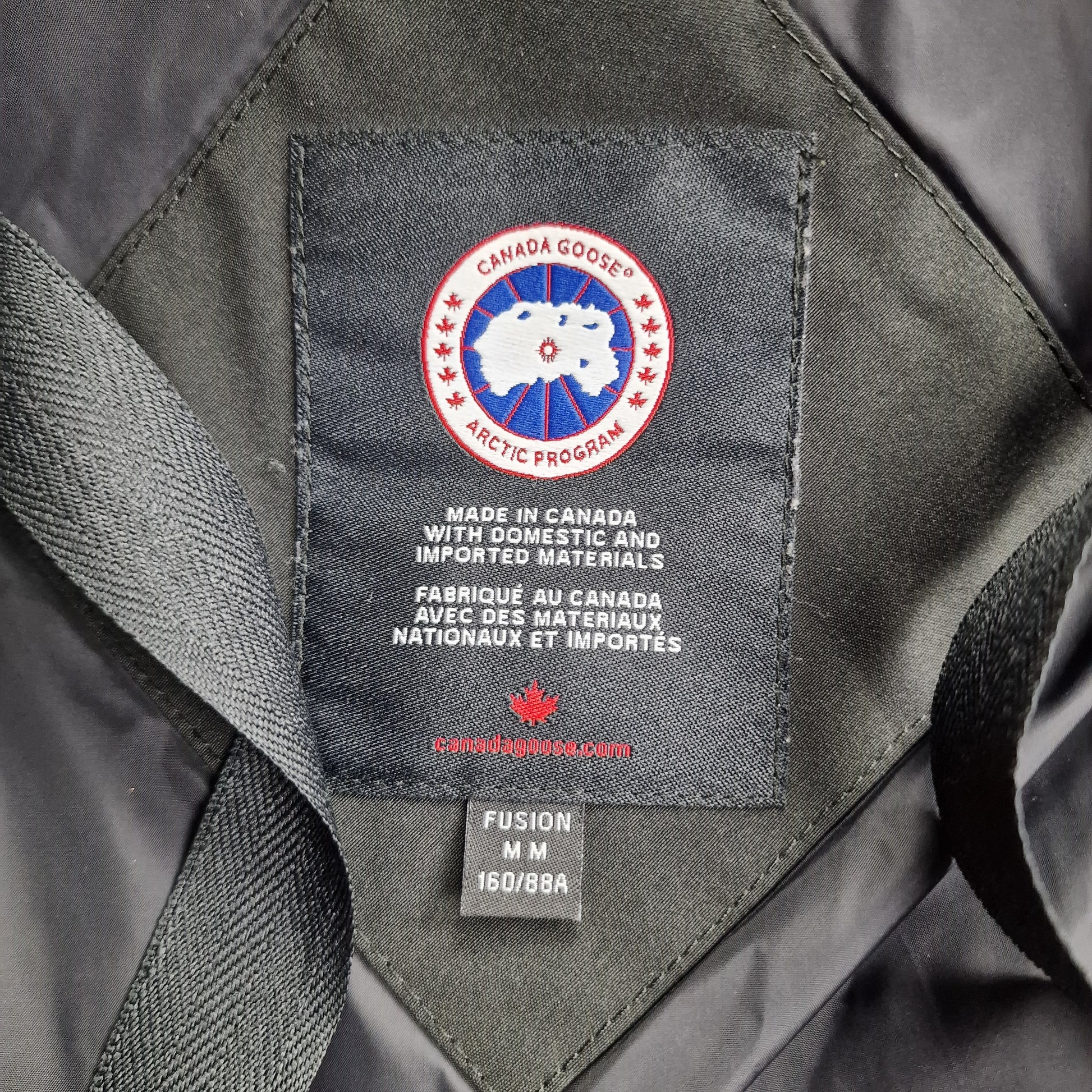 Close-up of authentic Canada Goose interior label showing Fusion fit, size M/M, Arctic Program badge, and Made in Canada certification