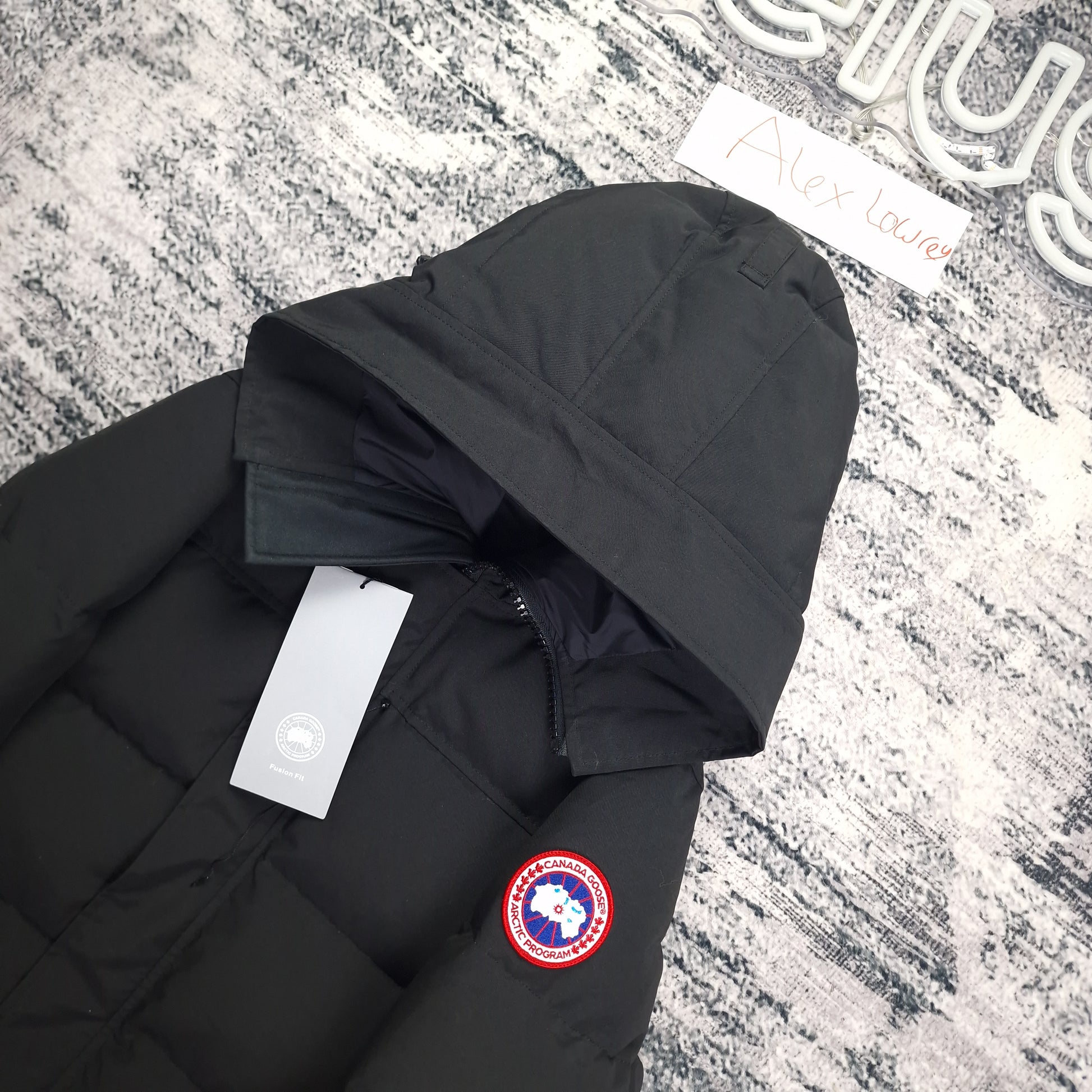 Close-up flat lay of Canada Goose Macmillan Parka 3804MA showing hood, authentic tags, and Arctic Program disc badge