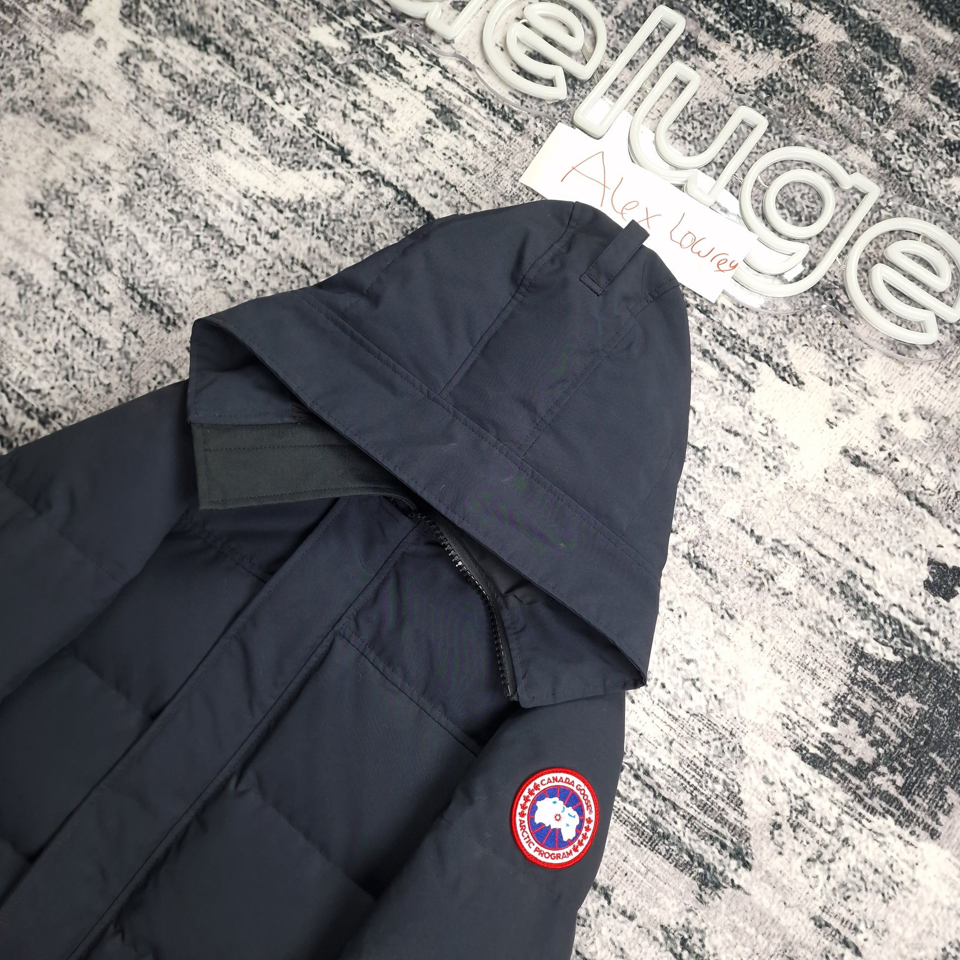 Close-up flat lay of Canada Goose Macmillan Parka 3804M showing navy hood construction and Arctic Program disc badge