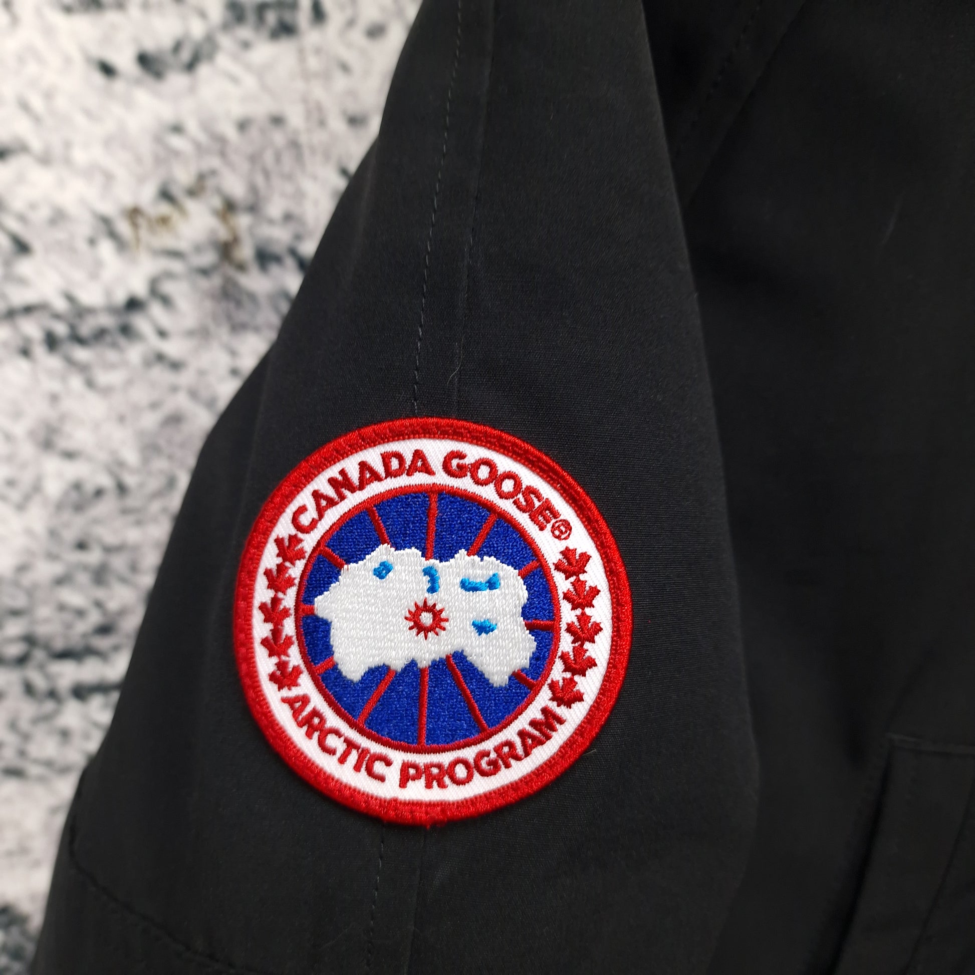 Close-up of authentic Canada Goose Arctic Program badge on Chilliwack Bomber 7950M, black colorway Small, showing iconic logo patch detail on men's luxury bomber jacket