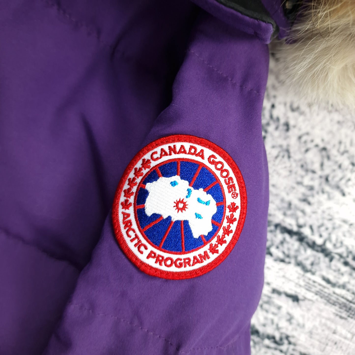 Close-up of authentic Canada Goose Arctic Program badge on Shelburne Parka 3802L, Purple Arctic Disk colorway, showing iconic logo patch detail on women's luxury winter jacket