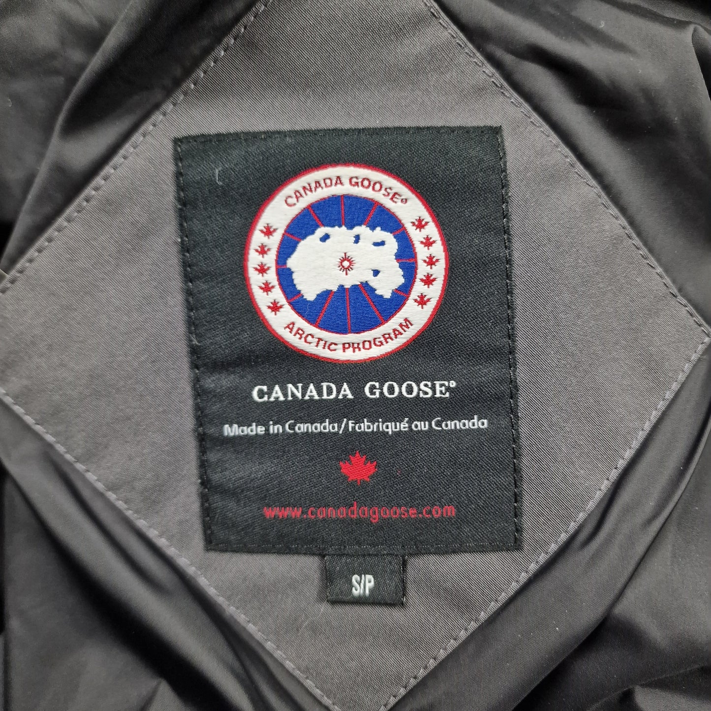 Close-up of Canada Goose necktag label inside Wyndham Parka 3808MA, showing authentic branding and size XS details for men's Graphite grey winter jacket