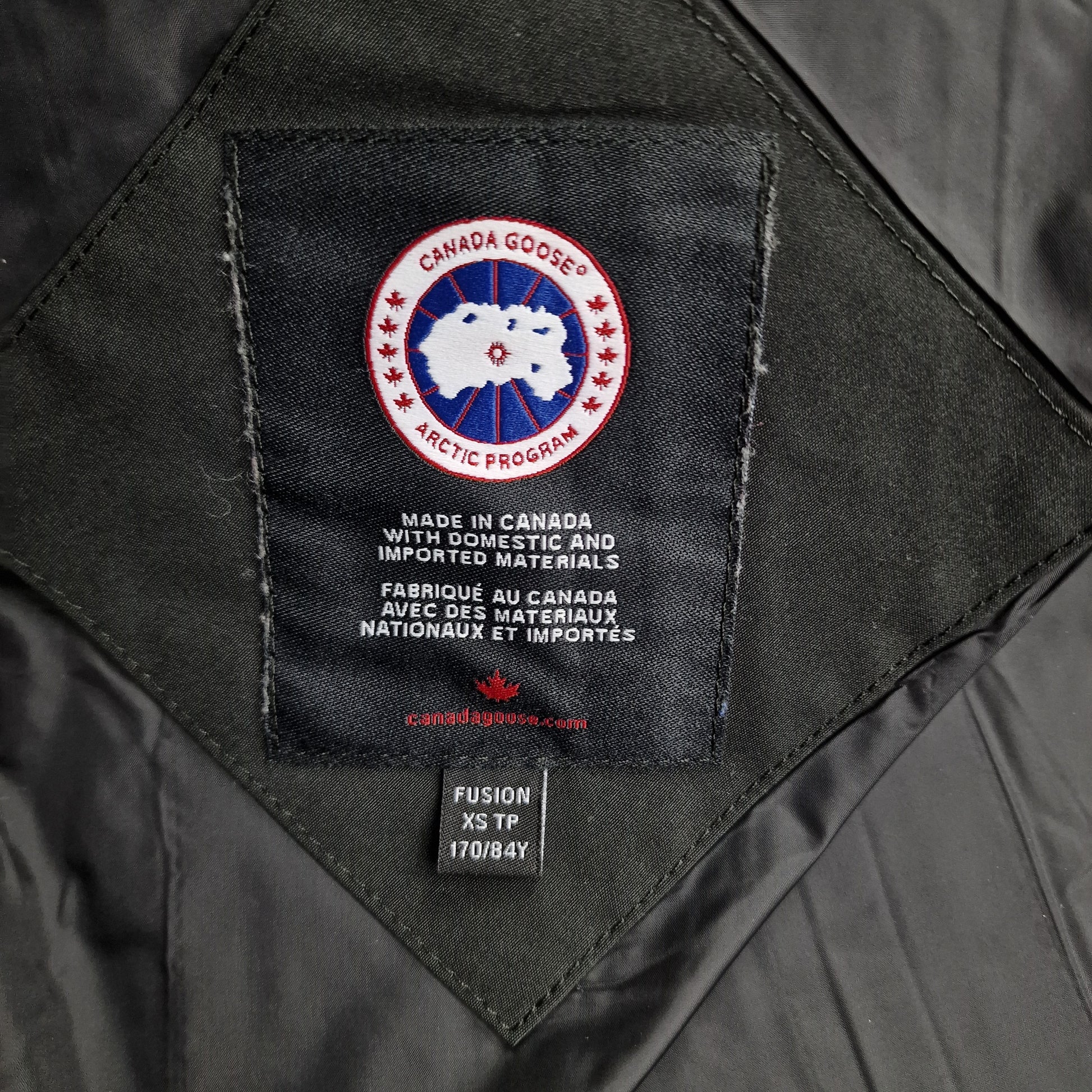 Close-up of Canada Goose necktag label inside Wyndham Parka 3808MA, showing authentic branding and size XS details for men's black winter jacket