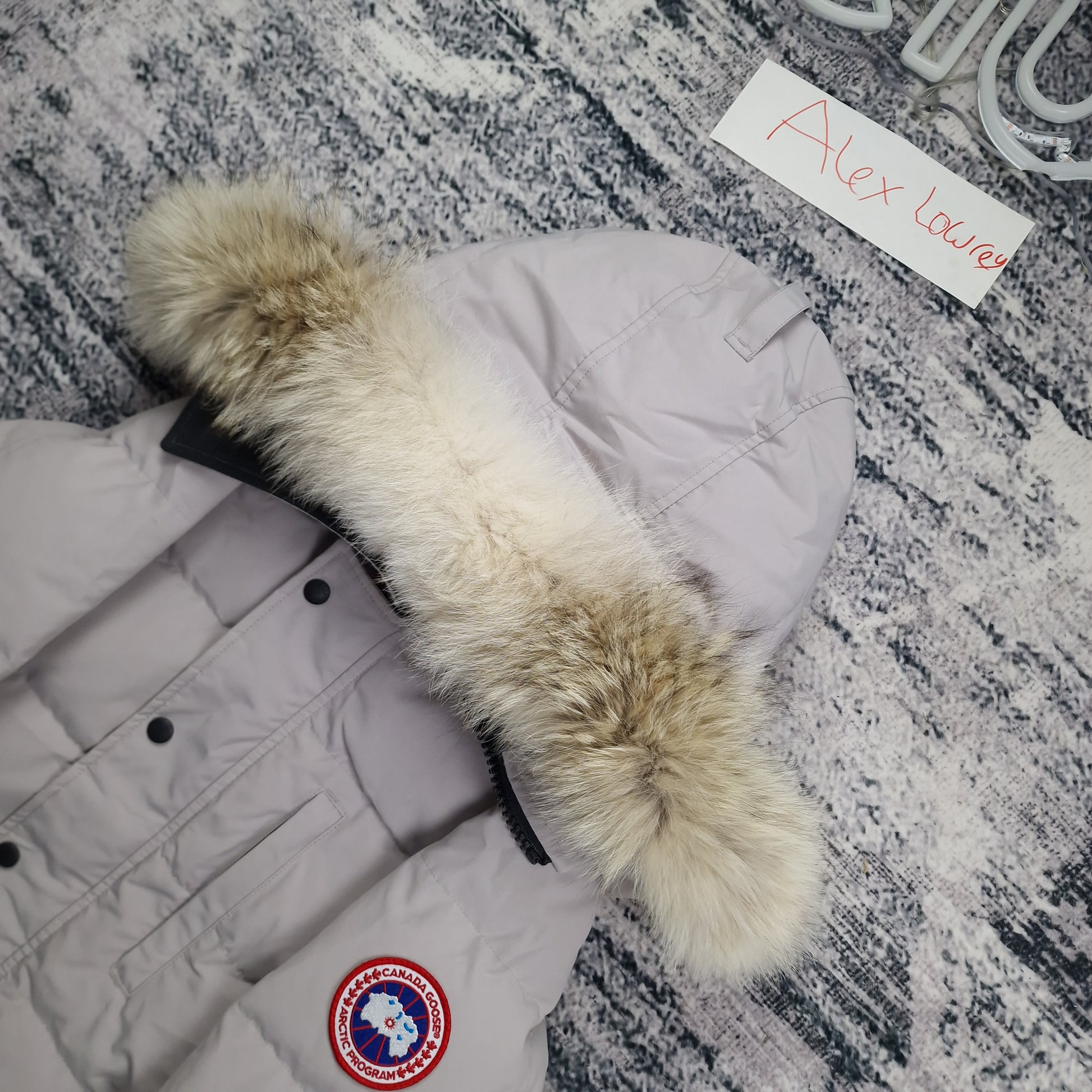 Close-up flat lay of Canada Goose Carson Parka 3805M showing luxurious coyote fur hood trim and Arctic Program disc badge in limestone