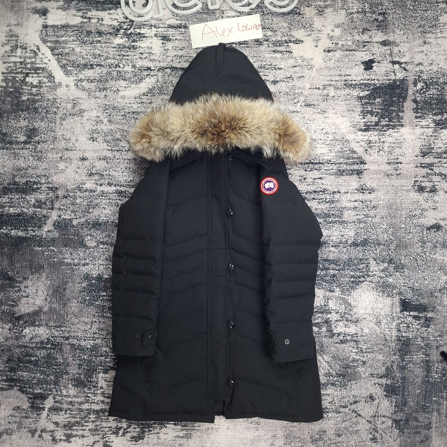 Front flat lay of black Canada Goose Lorette Parka women's medium with fur-trimmed hood, Arctic badge, and elegant knee-length design