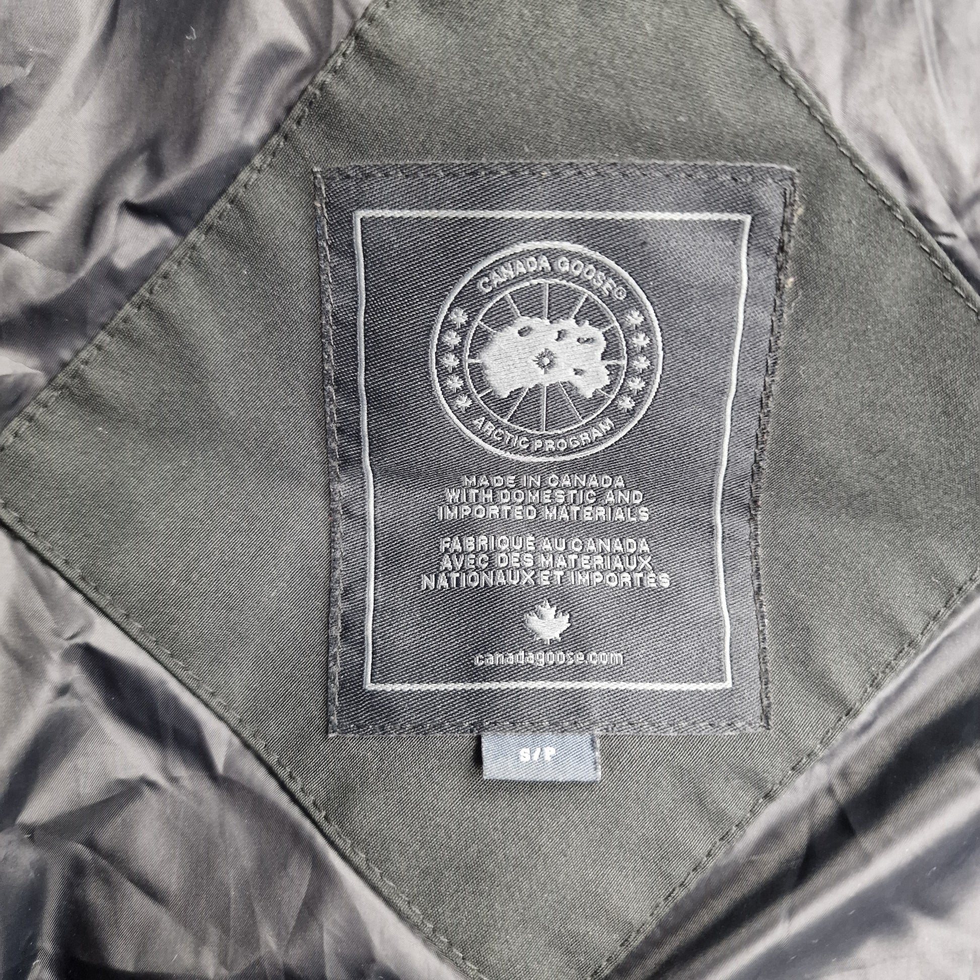 Close-up of authentic Canada Goose interior label showing size S, Arctic Program badge, and Made in Canada certification