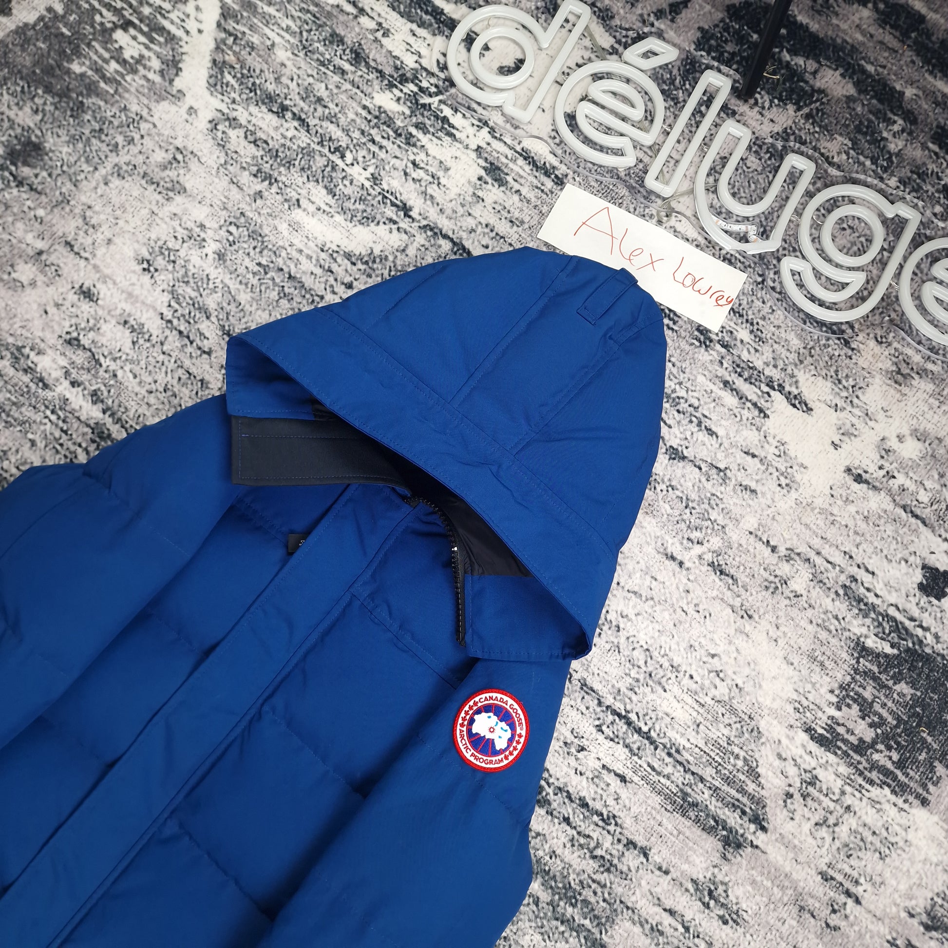 Close-up flat lay of Canada Goose Macmillan Parka Northern Night blue showing Arctic Program disc badge and hood construction detail