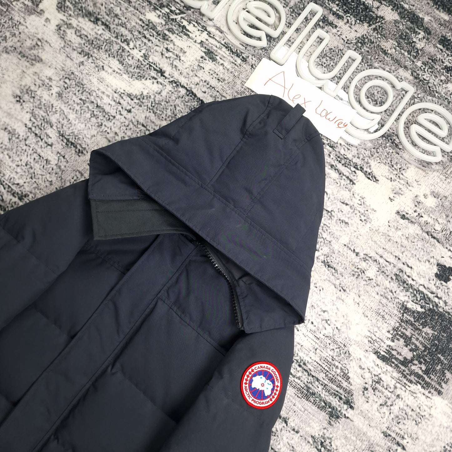 Close-up flat lay of Canada Goose Macmillan Parka 3804M showing navy hood construction and Arctic Program disc badge